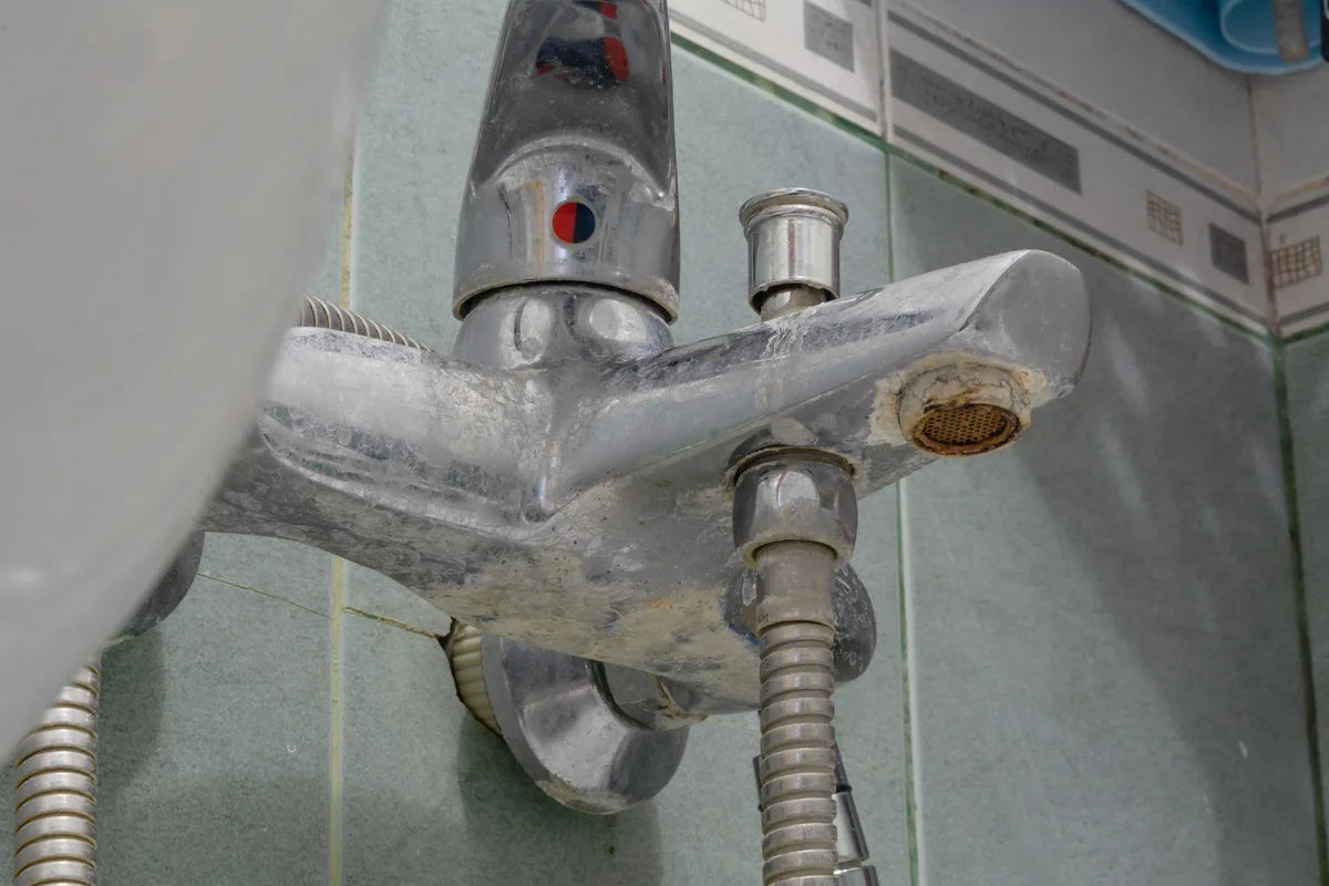 A chrome bath mixer tap encrusted with hard white limescale, with the outlet partly blocked